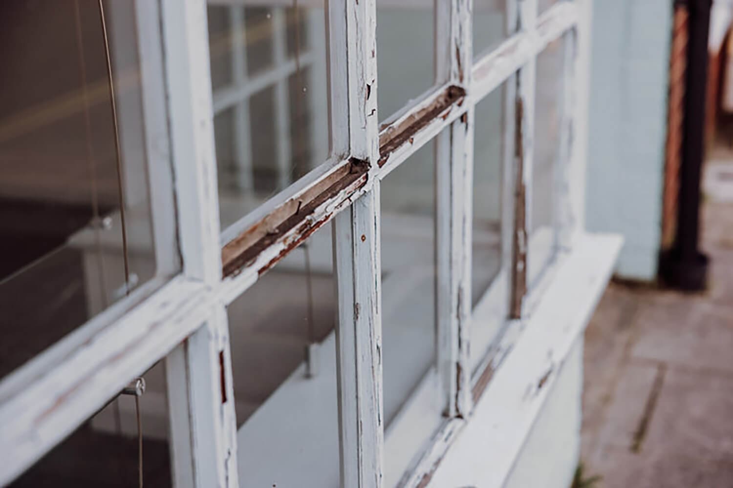 Peeling paint and deteriorating wood trim on an exterior window frame showing early signs of wood rot.